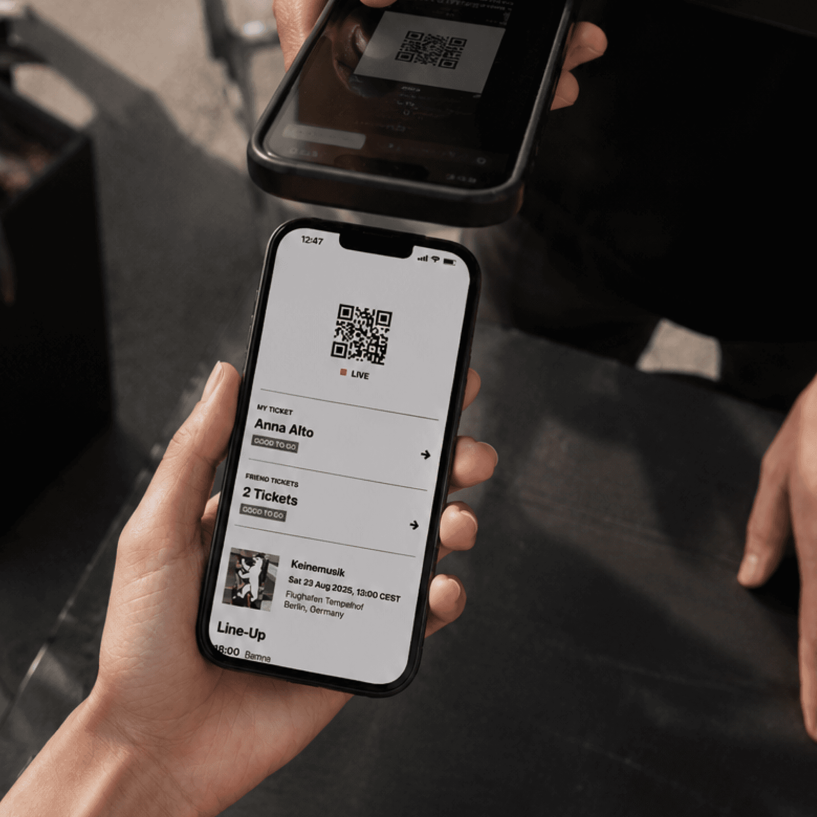 Eine Hand haelt ein Smartphone mit dem QR-Code eines Tickets, ein zweites Geraet scannt ihn von oben