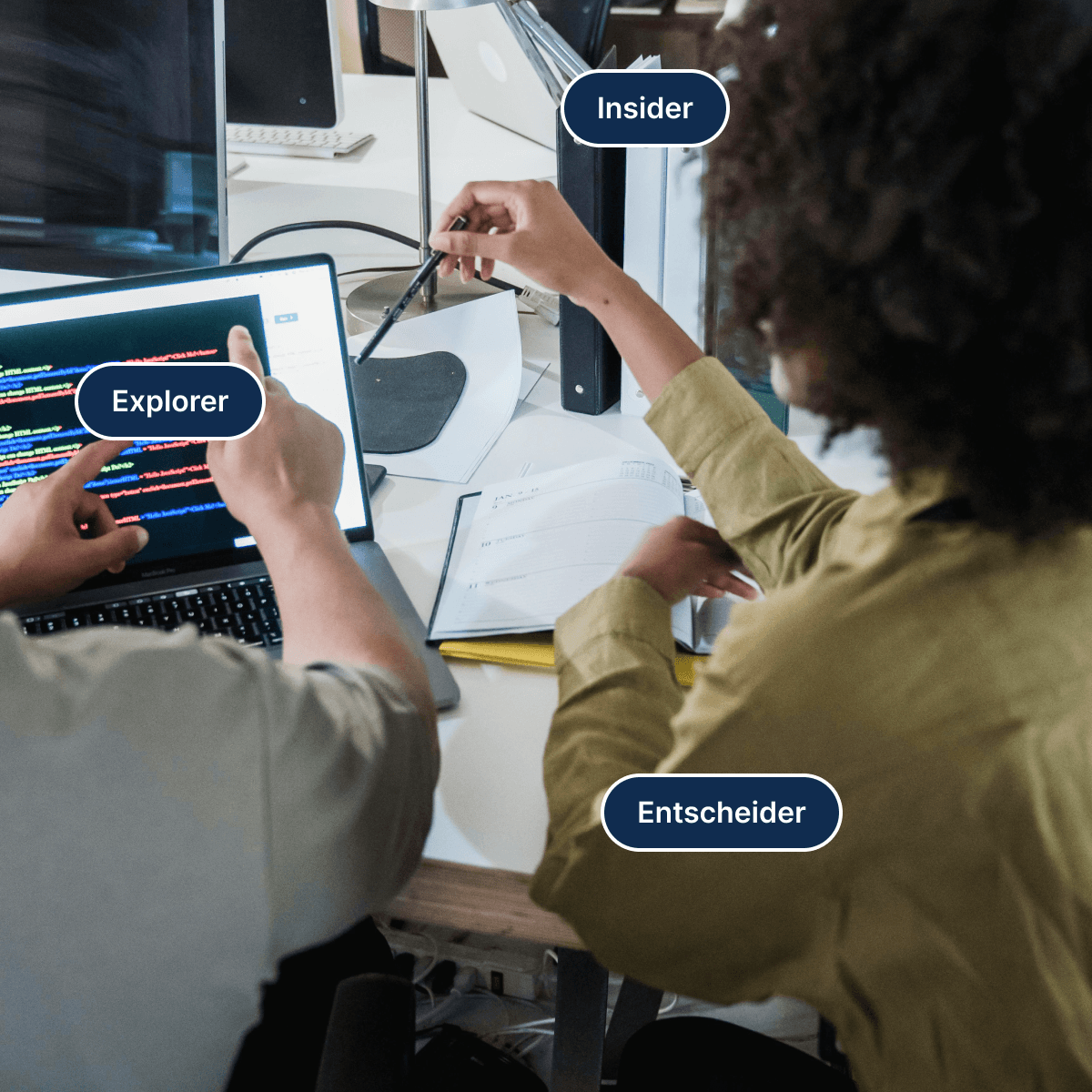 Zwei Personen an einem Schreibtisch vor einem Laptop mit Quelltext, darueber die Zielgruppen-Etiketten „Insider“, „Explorer“ und „Entscheider“