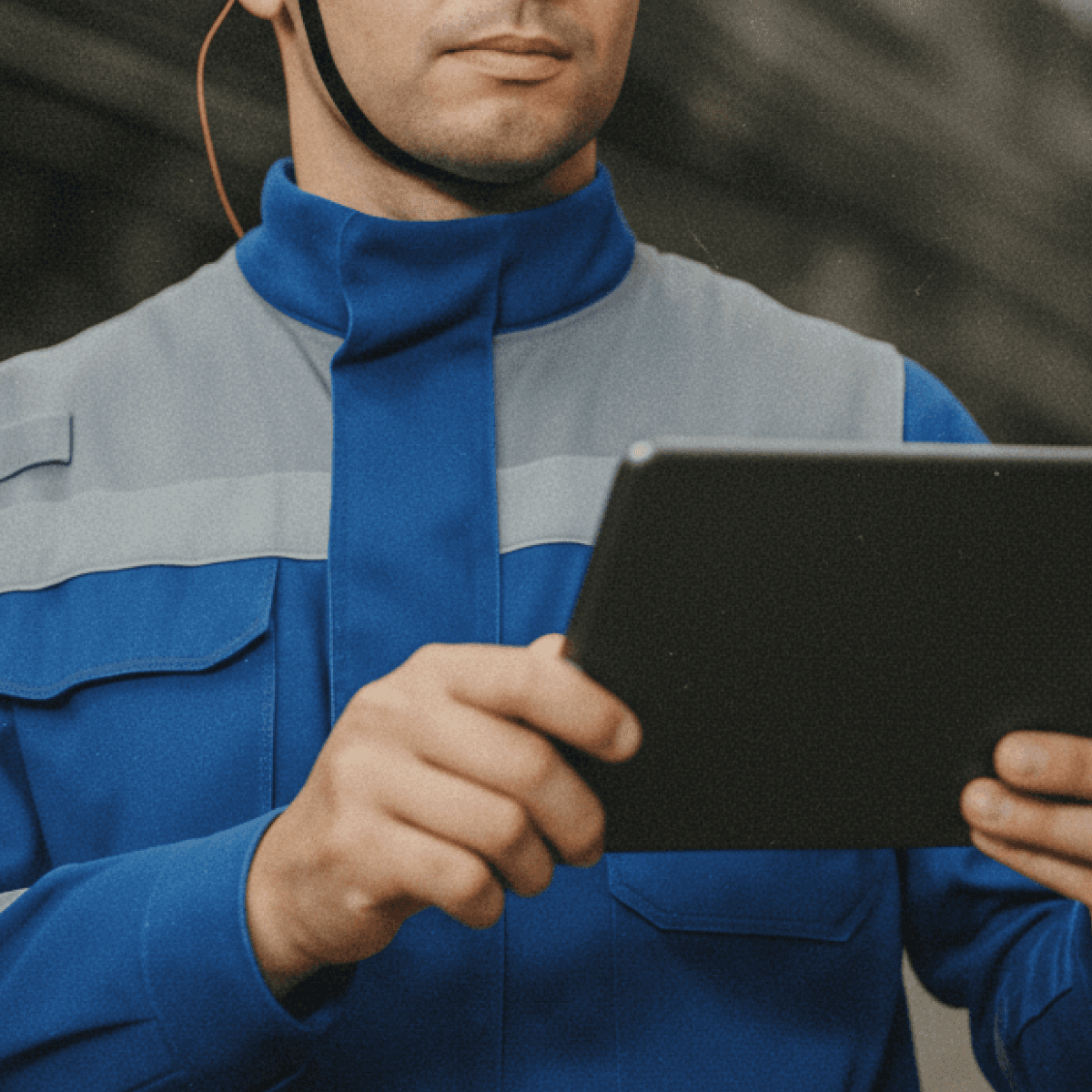 Mann in blauer Arbeitsjacke haelt ein Tablet in beiden Haenden
