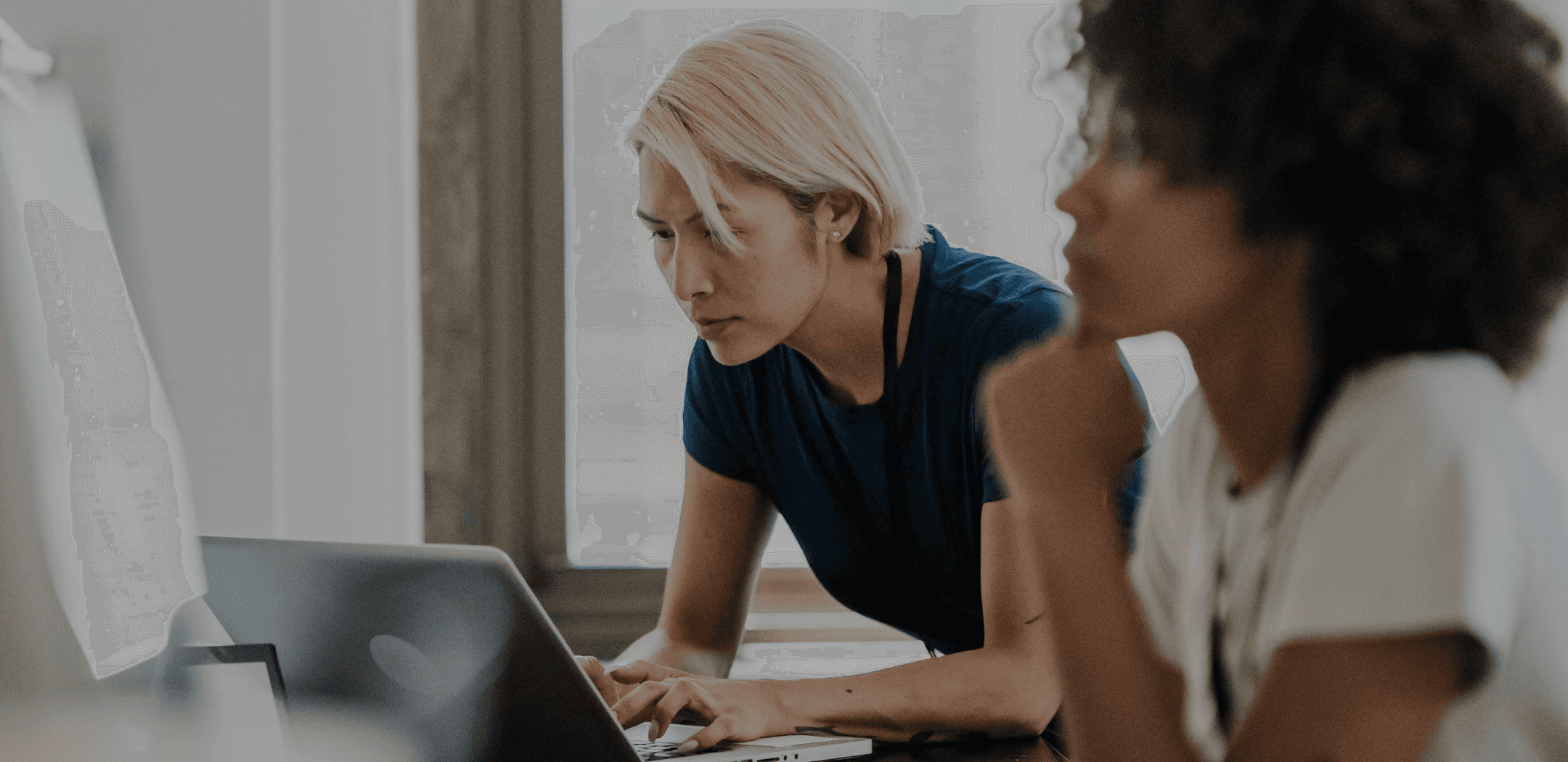 Zwei Frauen an einem Laptop: eine tippt, die andere sieht zu
