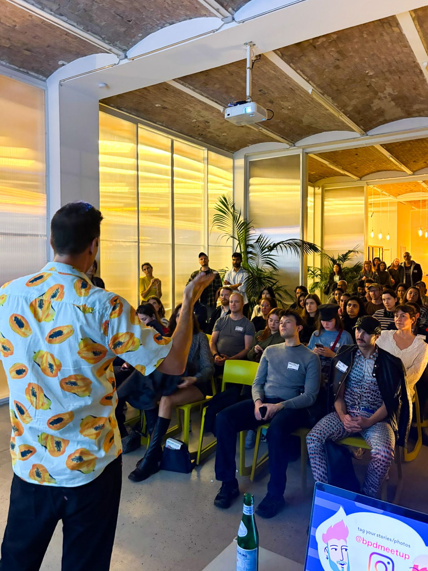 Breno Frias spricht vor vollem Saal im DAYONE Studio, das Publikum sitzt auf gelben Stühlen zwischen Backsteinwänden und Palmen